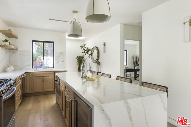 kitchen with light stone countertops, pendant lighting, beverage cooler, stainless steel appliances, and a breakfast bar area