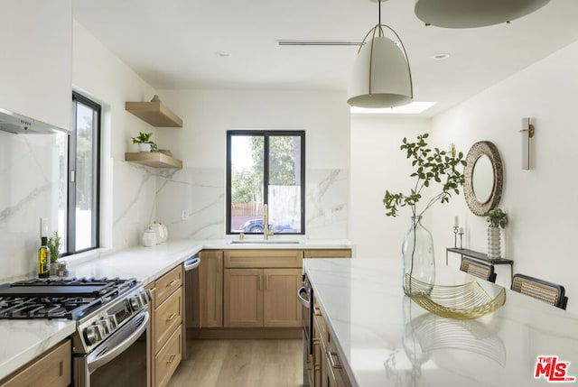 kitchen with stainless steel gas stove, sink, hanging light fixtures, decorative backsplash, and light hardwood / wood-style floors