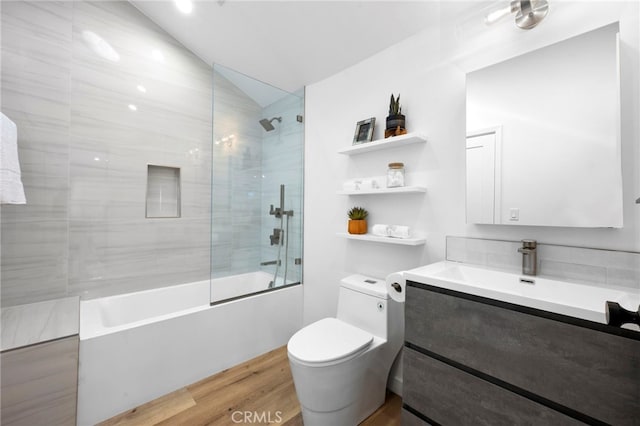 full bathroom with toilet, tiled shower / bath, wood-type flooring, vaulted ceiling, and vanity