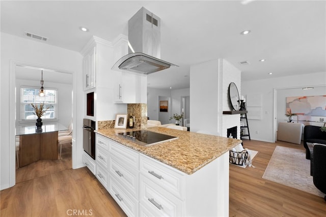 kitchen featuring a fireplace, light hardwood / wood-style floors, black appliances, white cabinets, and island range hood