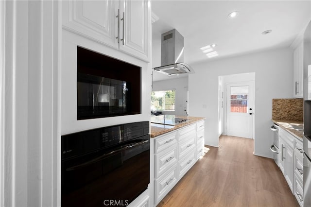 kitchen with black appliances, island exhaust hood, light hardwood / wood-style flooring, white cabinets, and light stone counters