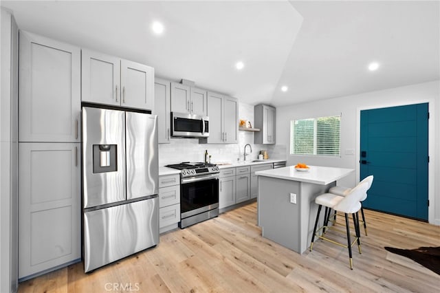 kitchen with a kitchen bar, gray cabinets, appliances with stainless steel finishes, a center island, and sink