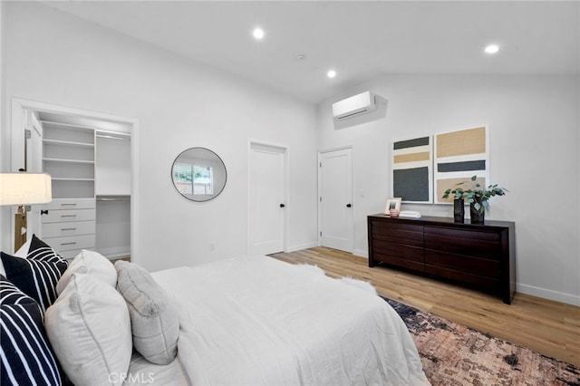 bedroom with lofted ceiling, light hardwood / wood-style flooring, a wall mounted air conditioner, a walk in closet, and a closet