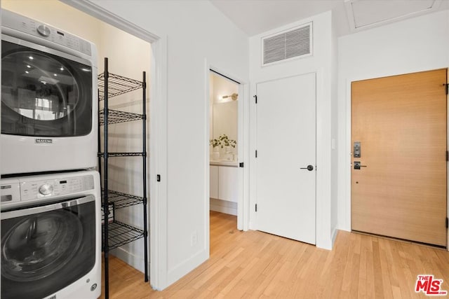 laundry area featuring stacked washer / drying machine and light hardwood / wood-style flooring