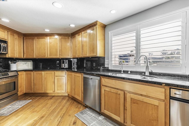 kitchen featuring appliances with stainless steel finishes, dark stone counters, a healthy amount of sunlight, sink, and light hardwood / wood-style flooring