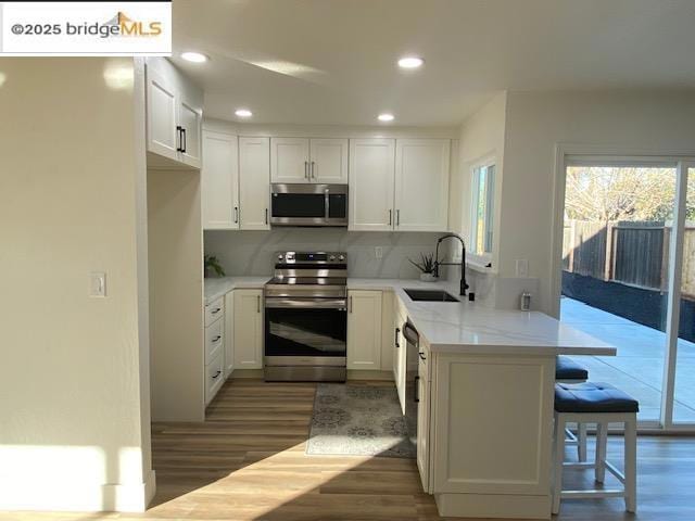 kitchen with kitchen peninsula, stainless steel appliances, white cabinets, and sink