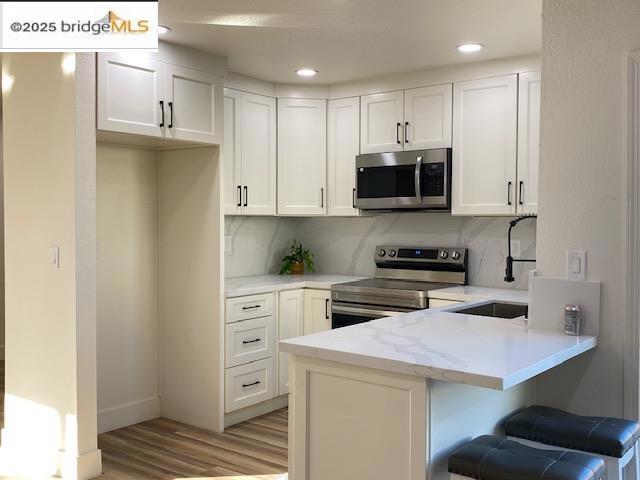 kitchen featuring stainless steel appliances, sink, white cabinetry, kitchen peninsula, and backsplash