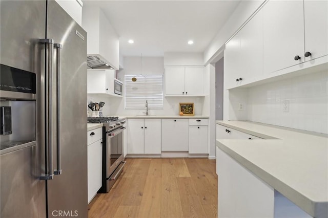 kitchen with kitchen peninsula, premium appliances, white cabinetry, and light hardwood / wood-style floors