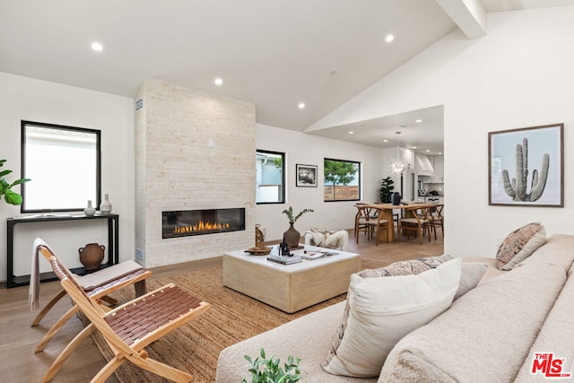 living room featuring high vaulted ceiling, light hardwood / wood-style flooring, a stone fireplace, and beamed ceiling