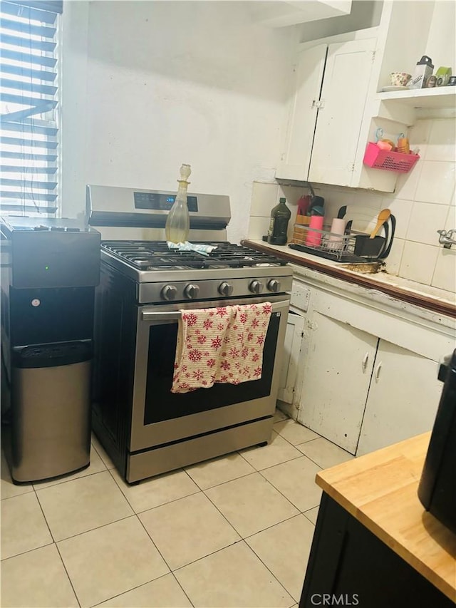 kitchen featuring light tile patterned floors, gas range, white cabinetry, and backsplash