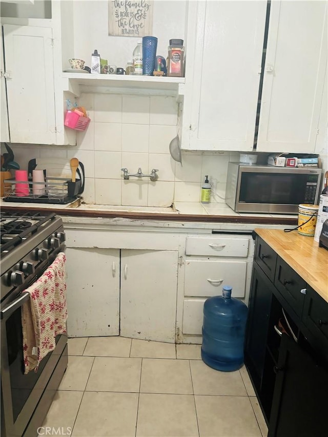 kitchen with appliances with stainless steel finishes, tasteful backsplash, light tile patterned floors, sink, and white cabinetry