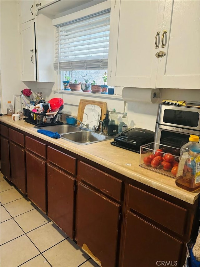 kitchen with white cabinetry, dark brown cabinets, sink, and light tile patterned floors