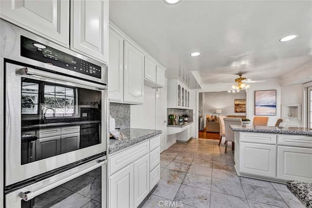 kitchen featuring white cabinets, ceiling fan, tasteful backsplash, dark stone counters, and double oven