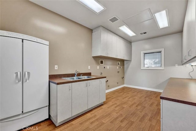 kitchen with sink, light hardwood / wood-style flooring, white cabinetry, and fridge