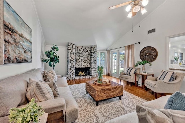 living room with french doors, light hardwood / wood-style floors, high vaulted ceiling, ceiling fan, and a stone fireplace