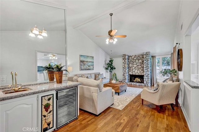 living room with a stone fireplace, wine cooler, light wood-type flooring, beam ceiling, and sink