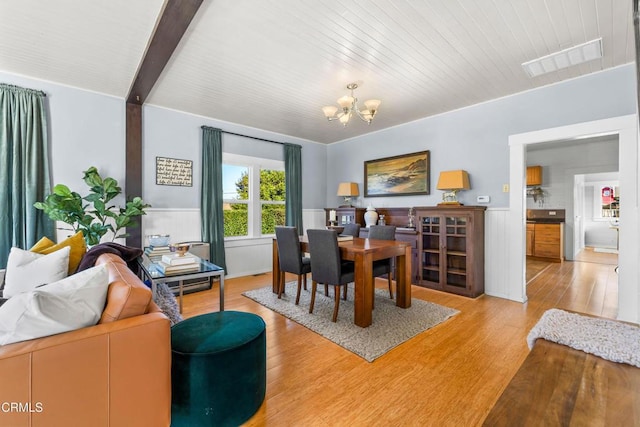 dining space featuring an inviting chandelier, light hardwood / wood-style floors, and beamed ceiling