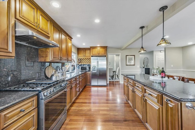 kitchen with pendant lighting, decorative backsplash, light wood-type flooring, stainless steel appliances, and dark stone counters