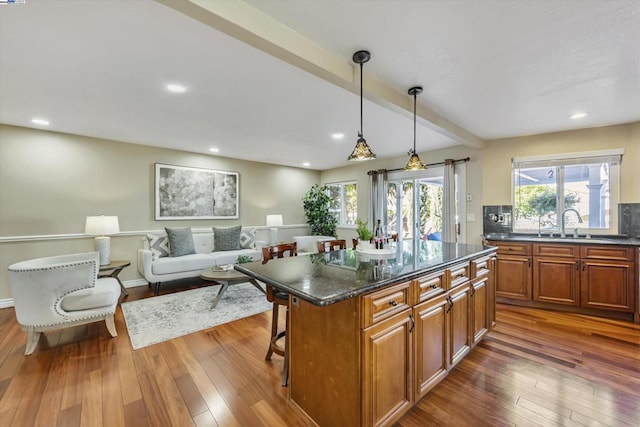 kitchen with pendant lighting, beam ceiling, a kitchen island, a breakfast bar area, and dark hardwood / wood-style flooring