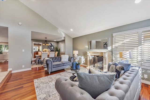 living room featuring high vaulted ceiling, a fireplace, wood-type flooring, and a notable chandelier