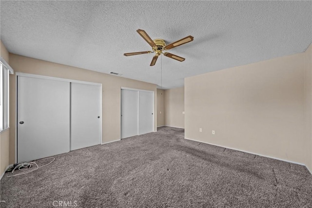 unfurnished bedroom featuring multiple closets, ceiling fan, a textured ceiling, and carpet floors