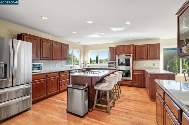 kitchen with appliances with stainless steel finishes, light hardwood / wood-style floors, a center island, a kitchen bar, and decorative backsplash