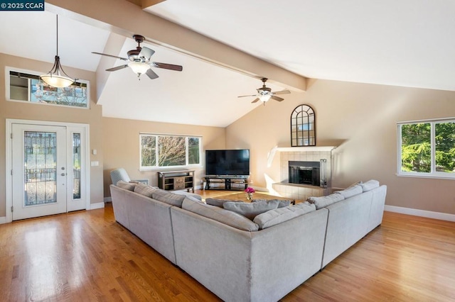 living room featuring a tile fireplace, light wood-type flooring, ceiling fan, and vaulted ceiling with beams