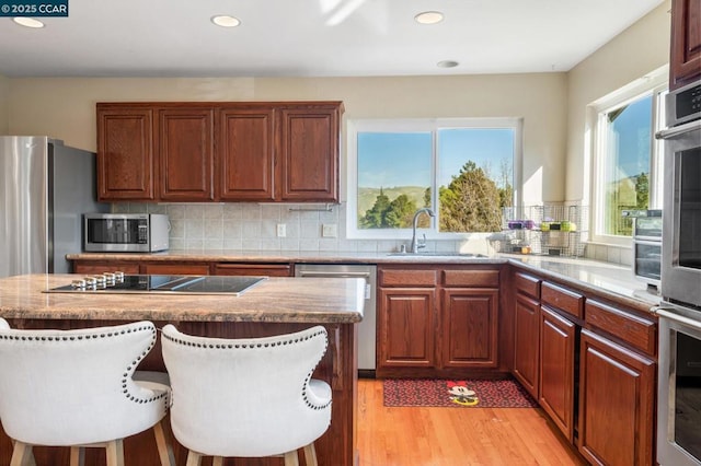 kitchen featuring a breakfast bar area, appliances with stainless steel finishes, light wood-type flooring, decorative backsplash, and sink