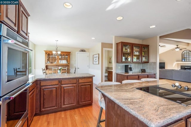 kitchen with hanging light fixtures, a breakfast bar, black electric cooktop, stainless steel double oven, and ceiling fan with notable chandelier