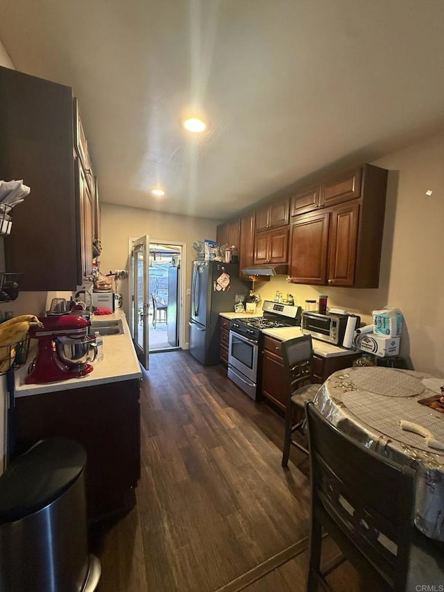 kitchen featuring under cabinet range hood, dark wood finished floors, stainless steel appliances, and light countertops