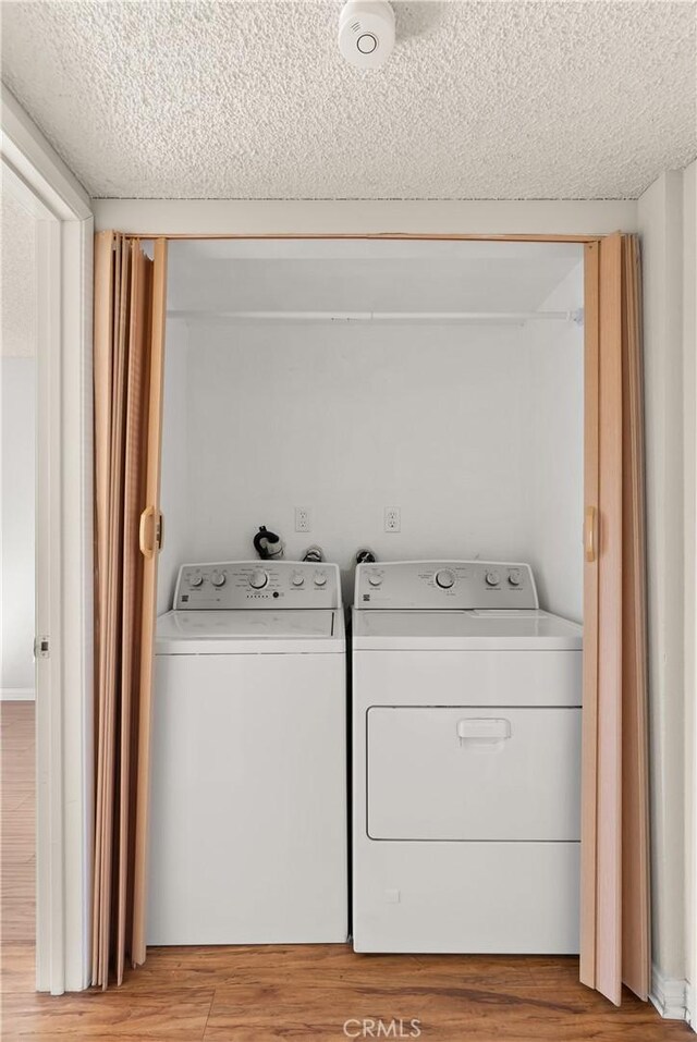 laundry area featuring light hardwood / wood-style floors, a textured ceiling, and washing machine and clothes dryer