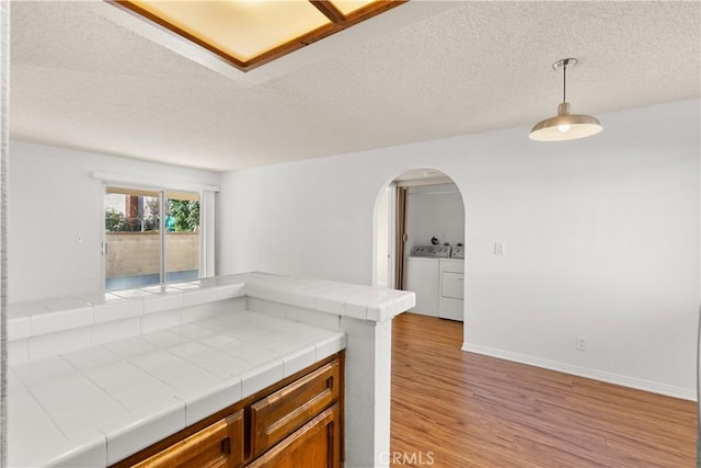 kitchen featuring hanging light fixtures, a textured ceiling, light hardwood / wood-style floors, washer and clothes dryer, and tile counters