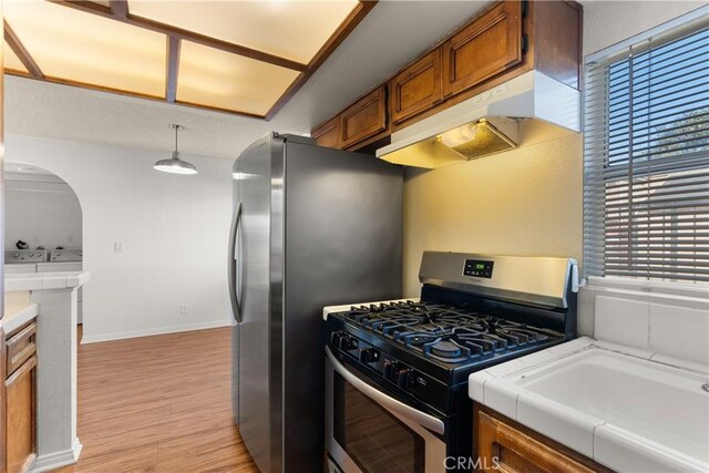 kitchen featuring stainless steel gas range oven, decorative light fixtures, a healthy amount of sunlight, and light hardwood / wood-style flooring