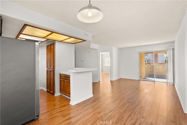 kitchen with decorative light fixtures, light hardwood / wood-style flooring, a textured ceiling, and stainless steel fridge