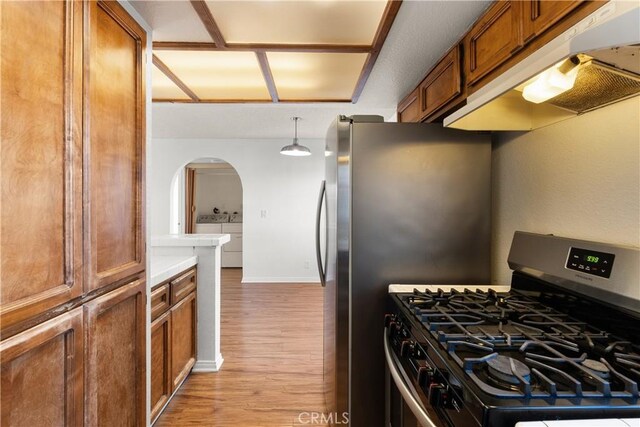 kitchen with stainless steel gas stove, light hardwood / wood-style flooring, washer and clothes dryer, and pendant lighting