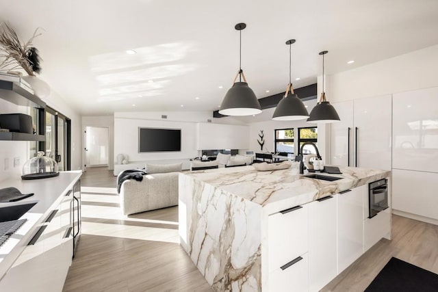 kitchen with sink, hanging light fixtures, white cabinets, and a kitchen island with sink