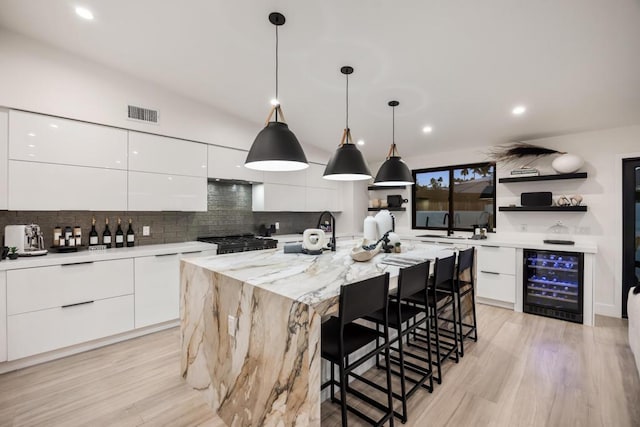 kitchen featuring a large island with sink, beverage cooler, white cabinets, and hanging light fixtures