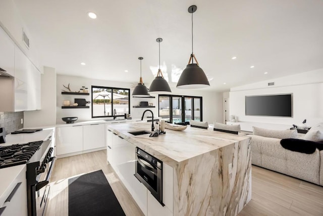 kitchen featuring white cabinetry, stainless steel range with gas cooktop, an island with sink, pendant lighting, and sink