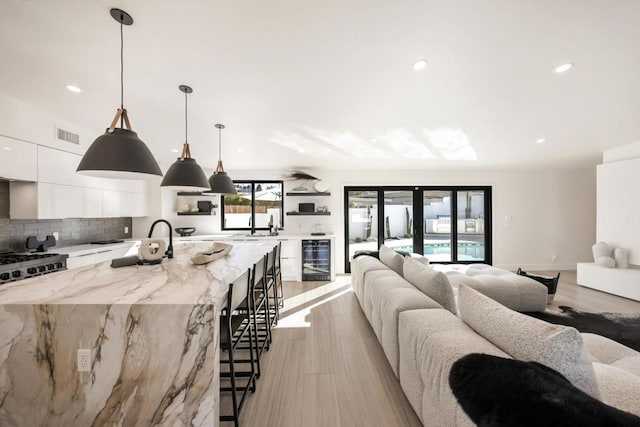 kitchen with a large island with sink, white cabinetry, a kitchen breakfast bar, hanging light fixtures, and light stone counters