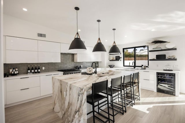 kitchen with decorative light fixtures, white cabinets, a center island with sink, and wine cooler