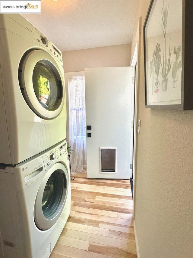 washroom with light hardwood / wood-style floors and stacked washing maching and dryer