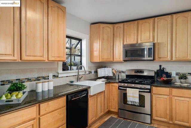 kitchen with sink, dark stone countertops, light brown cabinetry, backsplash, and appliances with stainless steel finishes