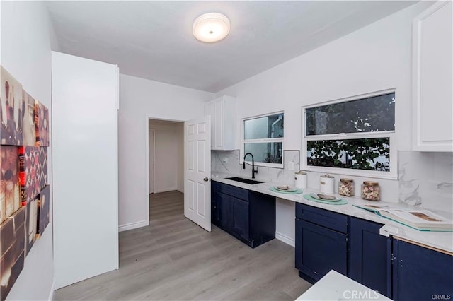 kitchen featuring backsplash, light wood-type flooring, blue cabinets, white cabinets, and sink