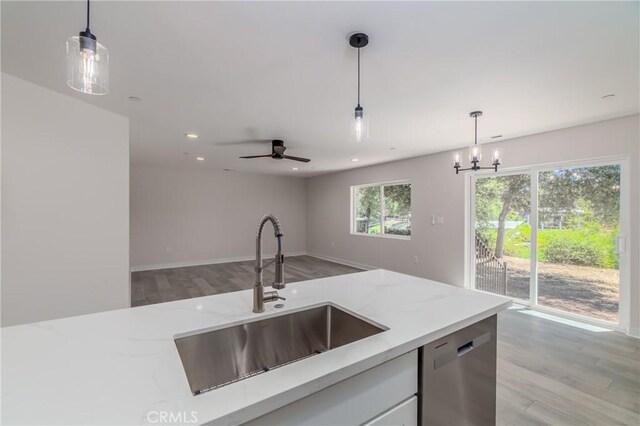 kitchen with light stone counters, dishwasher, decorative light fixtures, white cabinets, and sink