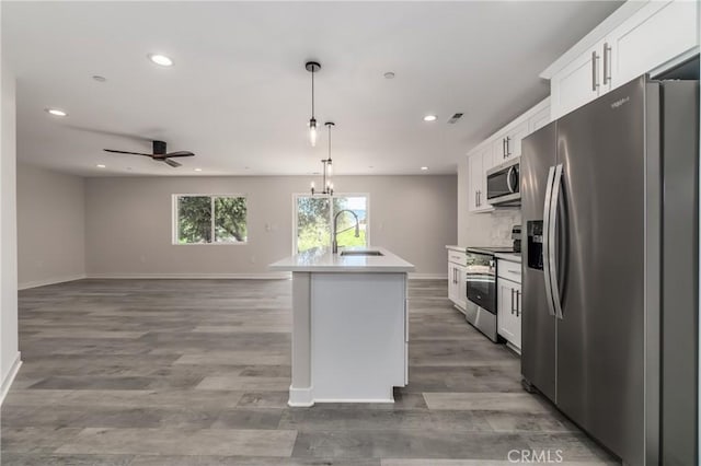 kitchen featuring sink, a kitchen island with sink, white cabinetry, hanging light fixtures, and stainless steel appliances