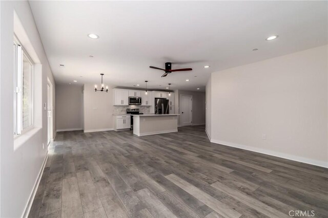 unfurnished living room with ceiling fan with notable chandelier and wood-type flooring