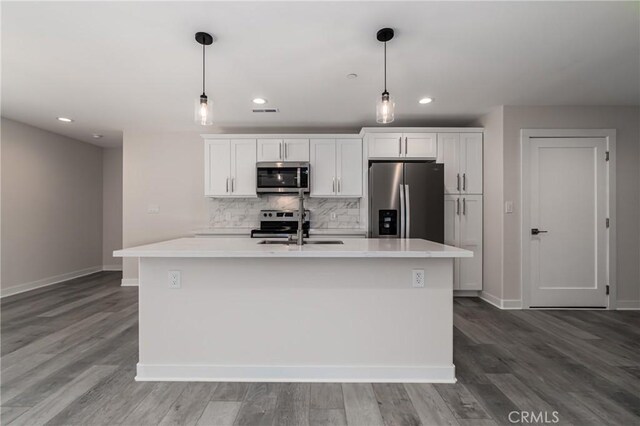 kitchen with decorative light fixtures, a center island with sink, white cabinets, and appliances with stainless steel finishes