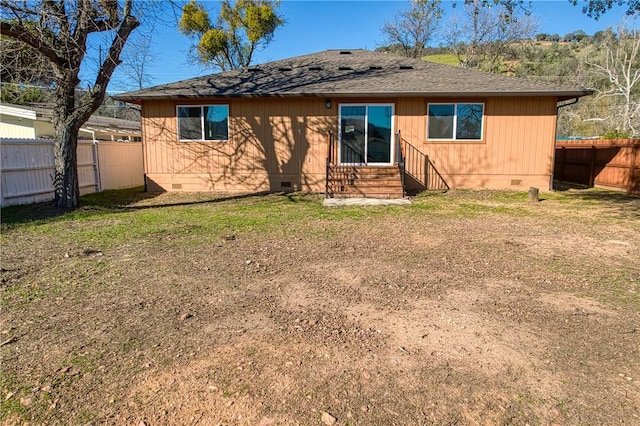 rear view of house with roof with shingles, a lawn, entry steps, crawl space, and a fenced backyard