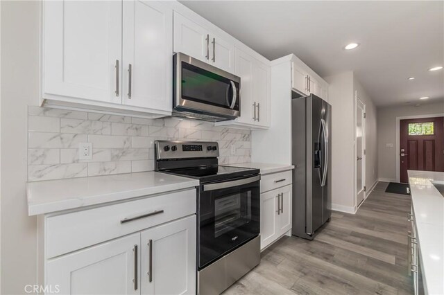 kitchen with white cabinets, light wood-type flooring, decorative backsplash, light stone countertops, and appliances with stainless steel finishes