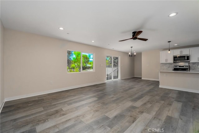 unfurnished living room with ceiling fan with notable chandelier, baseboards, dark wood finished floors, and recessed lighting